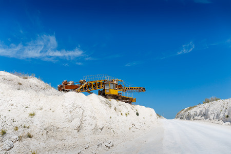 Yellow quarry heavy duty machine among white rocks in a mining quarry