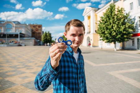Young man in blue shirt shows Fidget Spinner, selective focus on Spinner with blurred background for copy spaceの写真素材