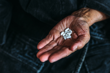 Handful of white tablets or pills in the hands of an elderly woman, copy spaceの写真素材