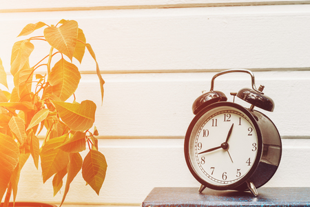 Round table clock - alarm clock on a white wooden wall background, sunlight effect, copy space