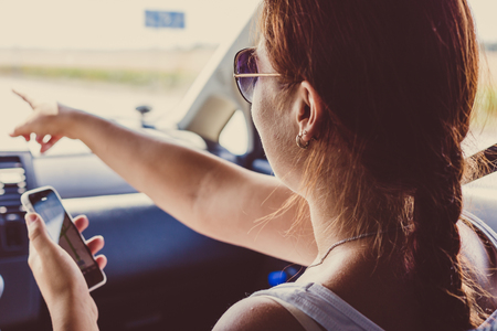 Girl on passenger seat in car holds mobile phone with map gps navigation and shows a hand forward, toned imageの写真素材