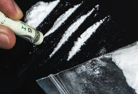 Hand of man holds rolled banknote for snorting line of cocaine powder. Problems with drugs conceptの写真素材
