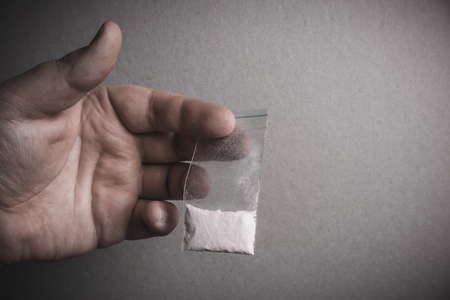 Mans hand holds plastic packet with cocaine powder or another drugs. Drug dealer selling drugs junkieの写真素材