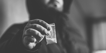 Drug dealer selling drugs junkie. Drug abuse concept and overdose concept. Mans hand holds plastic packet with cocaine powder, selective focus, black and white photoの写真素材
