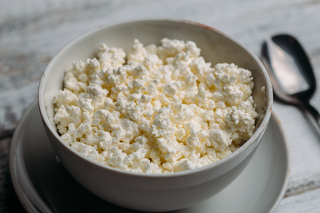 Cottage cheese or curd in bowl on white wooden rustic table, selective focus, close up. Healthy organic, diet and farm foodの写真素材