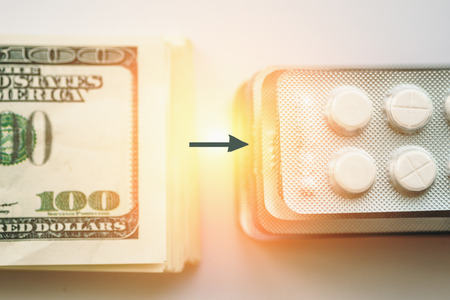 Bundle of money and  arrow to pack of medication tablets or drug pills, close-up. Expensive health care or money is health concept, selective focus, top view, tonedの写真素材