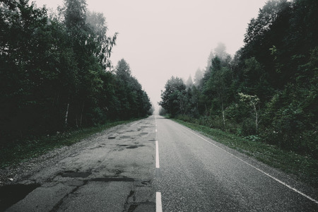 Morning fog, asphalt road in misty mountains, perspective, dark vintage tonedの写真素材