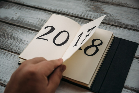 Man flips notepad sheet on a wooden table. 2017 is turning, 2018 is openingの写真素材