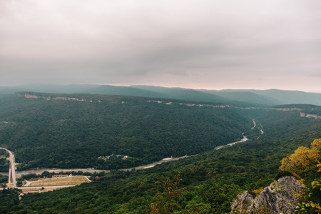 Panoramic view from mountain top to valley among rocks in low cloudy and foggy day, vintage toned