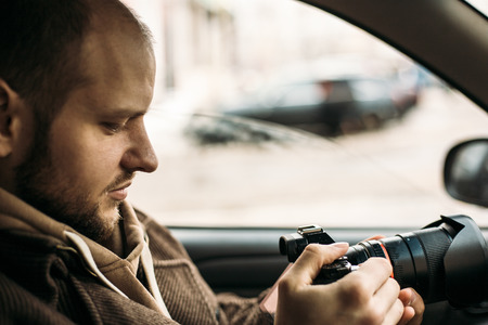 Investigator or private detective or reporter or paparazzi sitting in car and taking photo with professional camera, tonedの写真素材