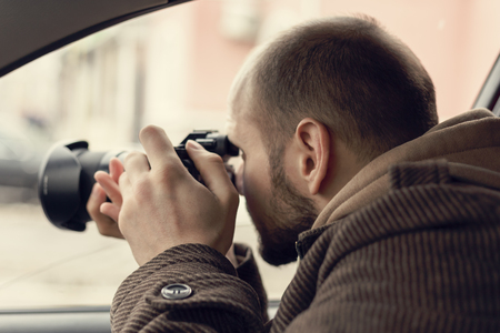 Investigator or private detective or reporter or paparazzi sitting in car and taking photo with...