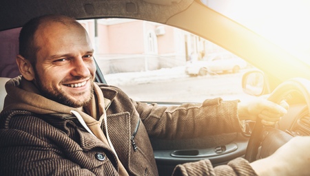 Handsome happy young driver smiling while driving his car in sun light effect, toned