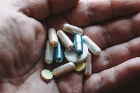 Male hand holding drugs or narcotic tablet and pills, addict ready to overdose, close up with...
