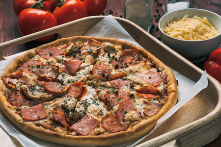 Pizza on wooden plate and food ingredients on kitchen table, tonedの写真素材