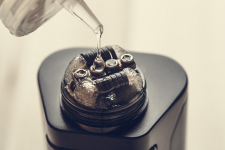 Rebuildable dripping atomizer or RDA for vaping or e-cigarette with coil and cotton stripes wetted with e-liquid, modern vape device for quit smoking, macro photo with selective focusの写真素材