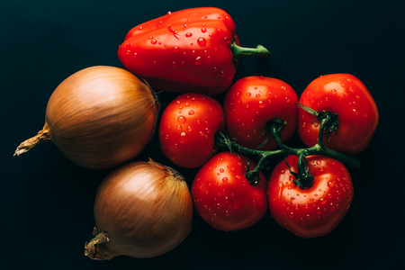 Fresh wet tomatoes in drops of water, golden onion, bell pepper on dark background, top viewの写真素材