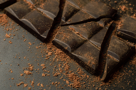 Broken chocolate bar to pieces and cocoa powder on dark background, macro shotの写真素材