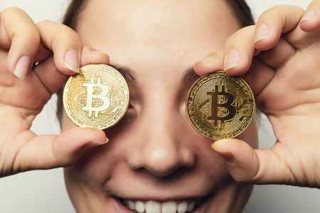 Young happy smiling girl holds Golden Bitcoin coins - symbol of cryptocurrency, new virtual moneyの写真素材