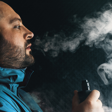 Vape man. Young guy vaping electronic cigarette or vape pen at black background