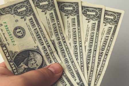 Male hand holding several one dollar bills, money is tight, poverty and bankruptcy concept, close up