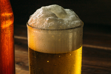 Glass of just poured beer with foam, close up