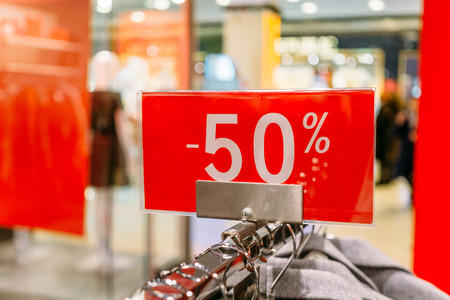 Sale 50 percent off letters on red banner inside popular fashion store with blurred mall background....