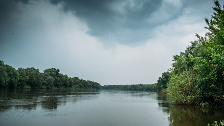 Rain and dramatic clouds over river and forest, panoramic photo