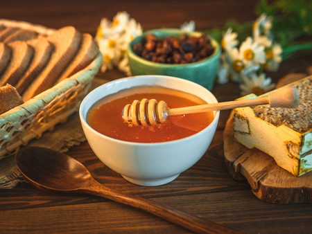 Honey pot and dipper at rustic table with bread, raisins, chamomile flowers and Honey combの写真素材