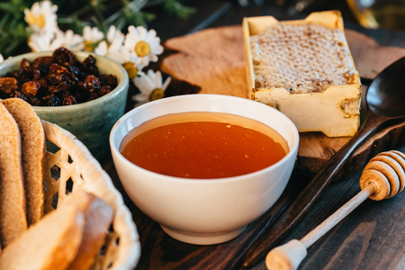 Honey in white ceramic bowl, honey dripper spoon, homemade honeycomb on rustic wooden table, close upの写真素材