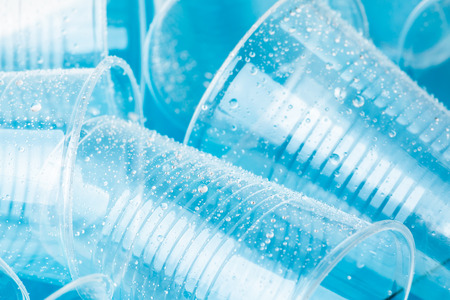 Empty transparent disposable plastic glasses in drops of water on bright blue background, close up