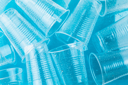 Empty transparent disposable plastic glasses in drops of water on bright blue background,  top view