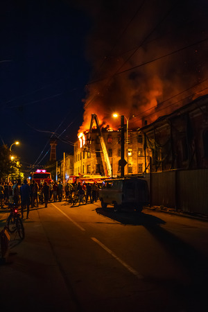 Night fire in apartment building, firefighters struggle with flame, silhouettes of unrecognizable people stand around. Fire disaster and accident tragedy concept, tonedの写真素材