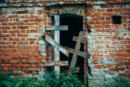 Two old wooden cross block the entrance to ancient antique tomb of brick in abandoned cemetery, tonedの写真素材