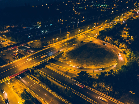 Aerial view to road junction with bridges and highways, modern city with night illumination and car traffic, drone photo from above, tonedの写真素材