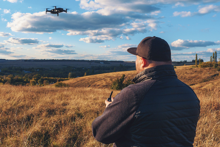 Man with remote controller operating flying drone or quad copter - modern small aircraft for aerial...