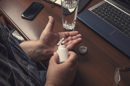 Senior man takes pills or medication tablets or drugs on hand from bottle at home, close upの写真素材