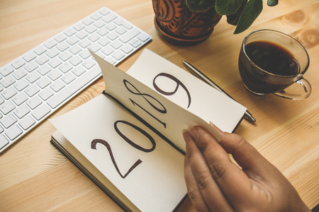 New Year 2019 is coming concept. Female hand flips notepad sheet on wooden table. 2018 is turning, 2019 is opening, tonedの写真素材