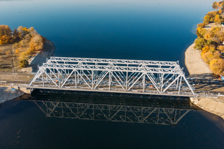 Aerial view drone shot of steel railroad bridge crossing big blue river, train transportation conceptの写真素材