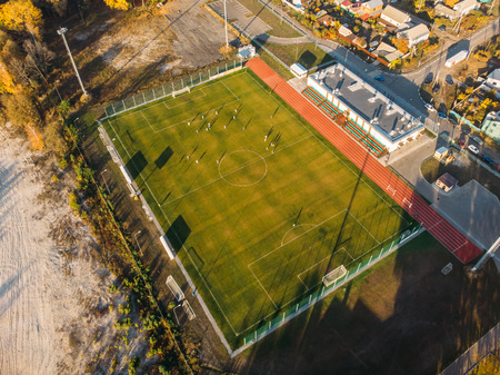 Aerial view of small soccer or football stadium with green lawn in city landscape, drone photo.