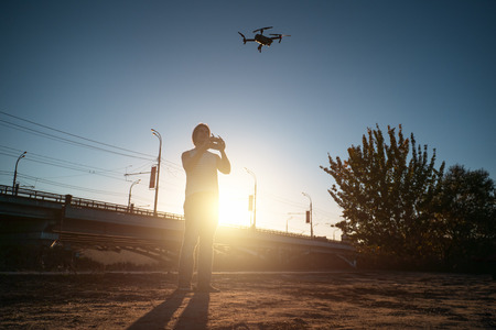 Man with remote controller operating flying drone or quad copter - modern small aircraft for aerial video making in city landscape at sunset, tonedの写真素材