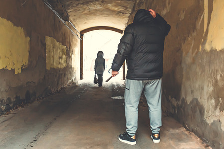 Robber or rapist criminal with knife in hand going to attack woman in urban tunnel, copy space,...
