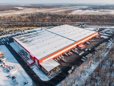 Aerial view of warehouse storages or industrial factory or logistics center from above. Top view of industrial buildings and trucks in winter landscapeの写真素材
