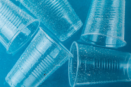 Disposable plastic cups in drops of water on a blue background, close upの写真素材