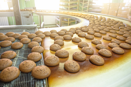 Bakery production line or with fresh sweet cookies on conveyor belt. Equipment machinery in confectionary factory workshop, industrial food production.の写真素材