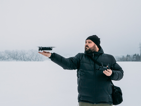 Man control drone and landing quadcopter on his hand at white winter background, toned