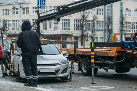 Tow truck with police officer loading, evacuating and arrest car for violation of parking low on city road.の写真素材