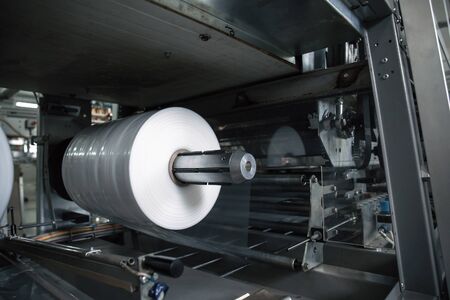 Plastic roll in industrial food packaging machine equipment tool at factory workshop, close up