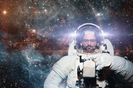 Astronaut in spaceman suit and helmet looks at camera at space background. People in space,...