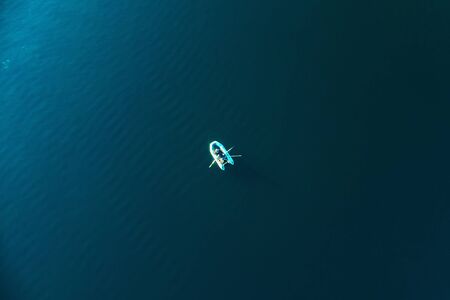 Boat with fisherman on blue sea water surface, aerial top view.