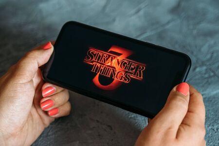Moscow, Russia - Circa August 2019 : Stranger Things 3 image logo on Iphone screen in woman hands, popular Netflix streaming TV series show season 3.のeditorial素材